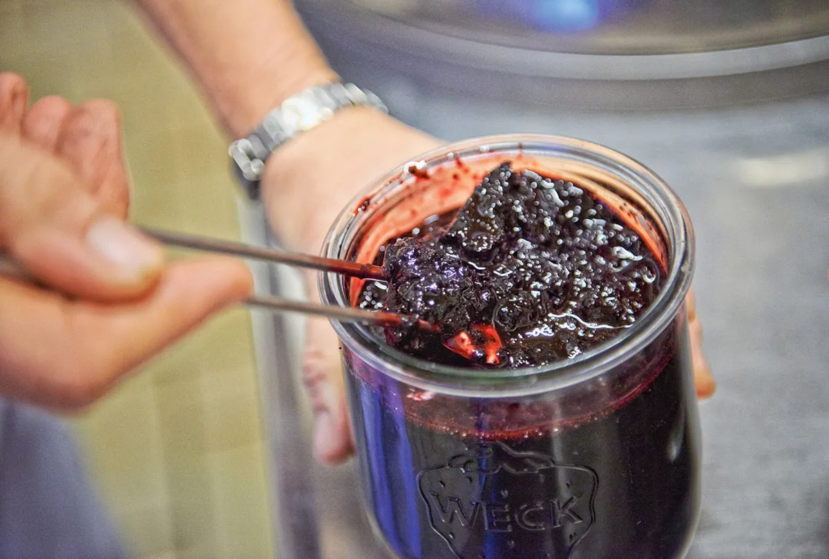 Dunkle Beeren werden mit einer Zange in ein Einmachglas gefüllt