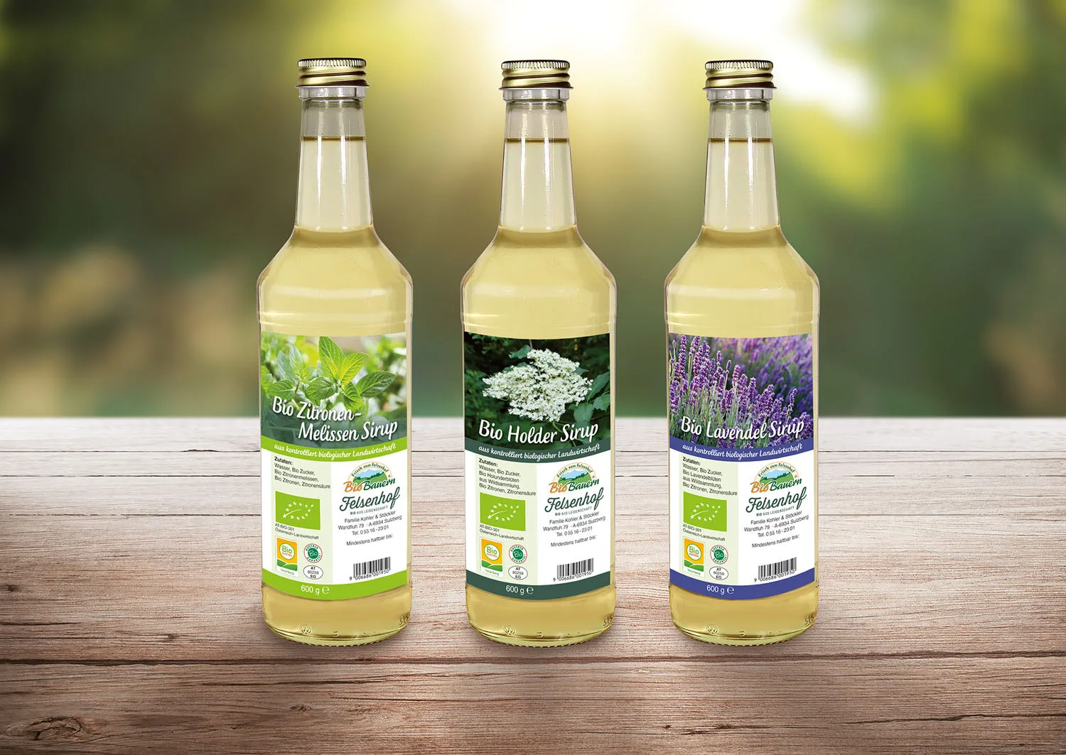Drei Flaschen Bio Sirup vom Felsenhof mit Melisse, Holunder und Lavendel auf einem Holztisch